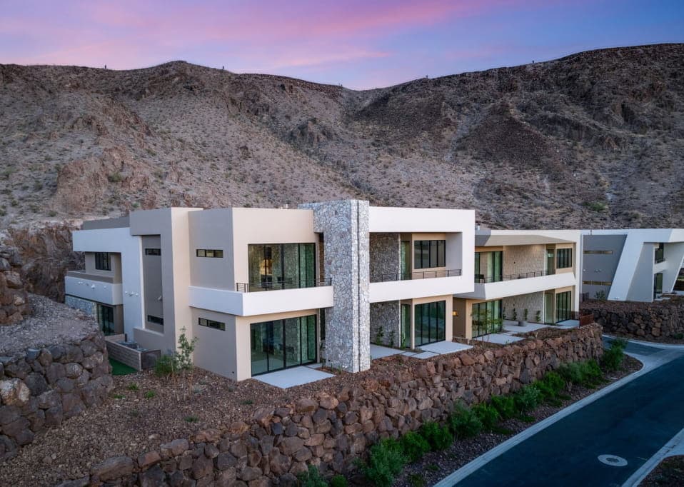 Modern luxury residence built into a desert mountainside, featuring contemporary architecture, stone accents, large windows, and terraced landscaping