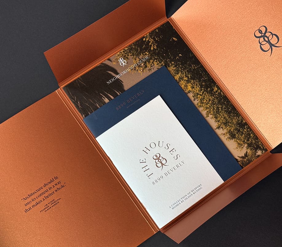Open copper-colored marketing folder containing printed real estate branding materials, including a booklet titled ‘THE HOUSES 8899 BEVERLY’ and a neighborhood guide, with elegant typography and imagery of palm trees visible.